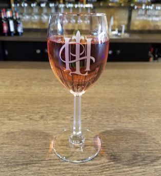 A glass of wine in a glass with the hook and ladder logo